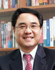 A person wearing a suit and tie in front of a book shelf  Description automatically generated